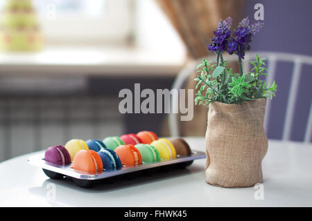 Colori assortiti e flawours macarons in una scatola di plastica su un tavolo in cafe accanto ai fiori di lavanda. Nizza bokeh cremoso e shallo Foto Stock