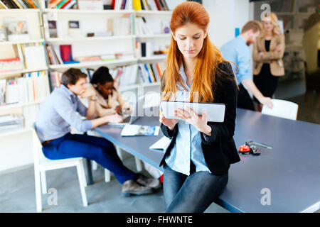 Imprenditrice azienda tablet in ufficio con i colleghi di lavoro comunicando in background Foto Stock