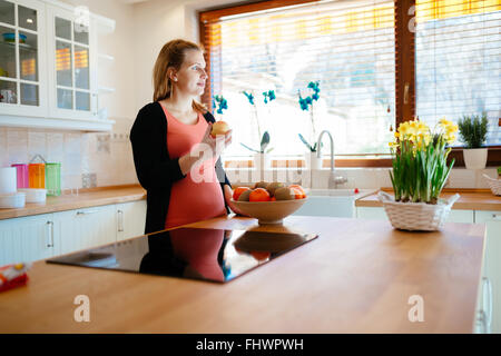 Donna incinta mangiare la frutta nella cucina moderna Foto Stock