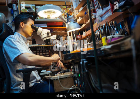 Gioielliere lavorando su metalli con dispositivo ottico che consente per lavori di precisione Foto Stock