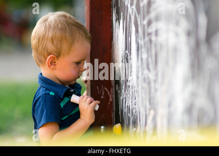 Creative toddler carino il disegno con chalk all'aperto su un tavolo da disegno Foto Stock