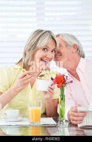 Senior uomo whispering segreto in felice womans orecchio Foto Stock
