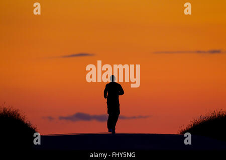 Pareggiatore solitario in esecuzione al tramonto stagliano contro il cielo arancione Foto Stock