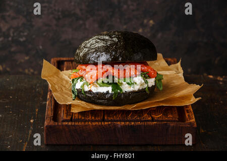 Nero hamburger di salmone con crema di formaggio e rucola scuro su sfondo di legno Foto Stock