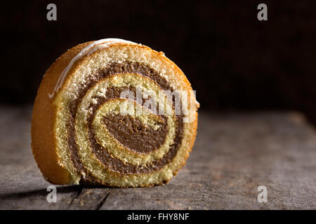 Rotolo di cioccolato torta con caramello e salsa alla vaniglia su sfondo di legno Foto Stock