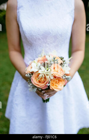 Sposa con un bel bouquet di pesca e rose bianche nelle sue mani Foto Stock