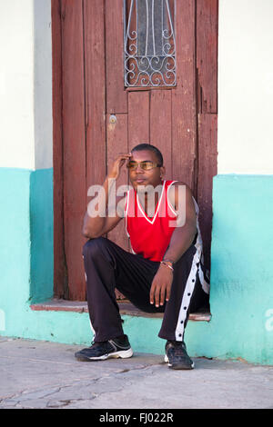 La vita quotidiana a Cuba - giovani cubani l uomo con gli occhiali seduto sulla porta di casa a porta a Cienfuegos, Cuba, West Indies, dei Caraibi e America centrale Foto Stock