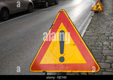 Rosso brillante e triangolo giallo cartello stradale con un punto esclamativo sul ciglio della strada Foto Stock