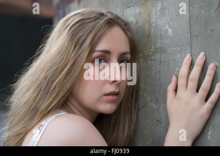 Spaventata giovane donna appoggiata contro il muro Foto Stock