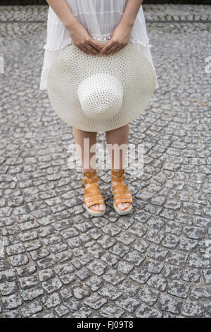 Close up della donna che mantiene un cappello in piedi sul lastricato della strada Foto Stock