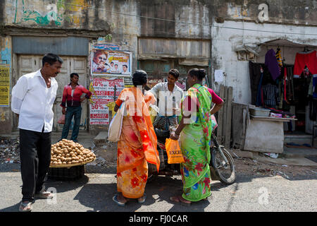 Un gruppo di indiani in piedi e parlare intorno a una motocicletta davanti ai negozi lungo la strada vicino a Chennai Foto Stock