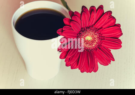 Rosso fiore di gerbera e tazza di caffè sulla scrivania in legno. Messa a fuoco selettiva, tonica Foto Stock