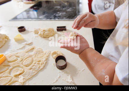 I bambini con le mani in mano impastare la pasta per i biscotti di cottura, pasta di farina, teglie su un tavolo bianco in background. Foto Stock