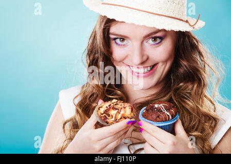 Panificio, cibo dolce e concetto di persone. Closeup sorridente estate donna capelli ricci cappello di paglia contenere dolci tortine in mani su blu Foto Stock