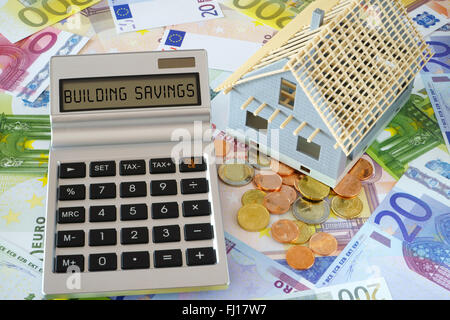 Calcolatrice tascabile con le parole la costruzione di risparmi sul display. Il modello di un nuovo edificio. In background molti le banconote in euro Foto Stock