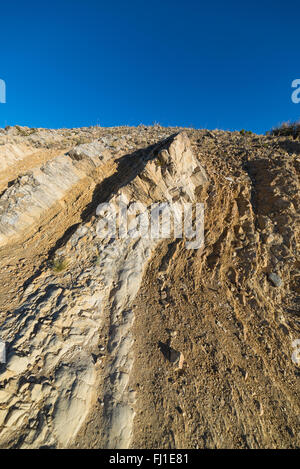 Close up di antiche rocce sedimentarie stratificate sperone di roccia, piegata dal potere di geologici movimento crostale. Cielo blu chiaro. Foto Stock