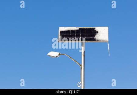 Energia Solare luce di strada con la neve e il ghiaccio sul cielo blu sullo sfondo Foto Stock