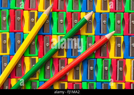 Righe colorate di rosso, giallo, verde e blu in plastica temperamatite con giallo verde e rosso e matite che necessitano di affilatura Foto Stock
