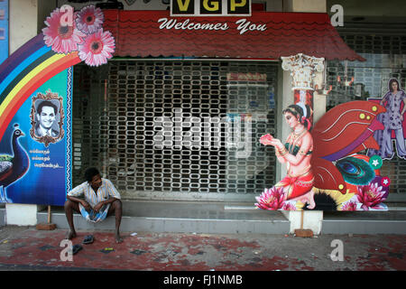 Uomo seduto da solo sulla strada guardando il segno che rappresenta una bella donna o dea o angel in una strada di Chennai, India Foto Stock