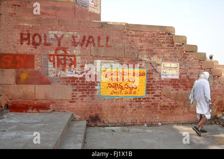 Un uomo cammina da solo lungo una parete con "parete santo' iscritto nella città santa Varanasi, India Foto Stock