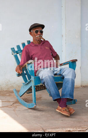 Vita quotidiana a Cuba - uomo cubano che fuma sigaro in vecchia sedia a dondolo tradizionale sul portico a Vinales, Pinar del Rio Provincia, Cuba, Indie Occidentali Foto Stock