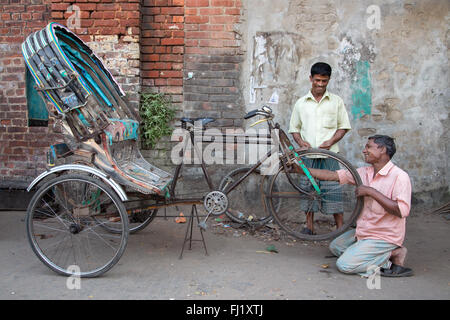 Un uomo sorridente riparazioni / modifiche un rickshaw pneumatico sgonfio con soddisfazione del cliente , Chittagong, Bangladesh Foto Stock