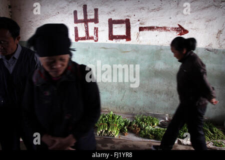 Le donne nel mercato Yuanyang con freccia dipinta su un muro per mostrare la direzione, Yuanyang, Cina Foto Stock