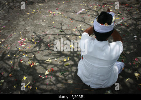 Uomo indù in preghiera sul pavimento con l'ombra di un albero e petali di fiori in Ubud , Indonesia Foto Stock