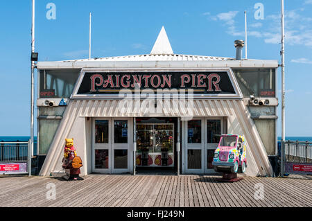 La luce diretta del sole sottolinea i bambini passeggiate al di fuori di un grande padiglione di alloggiamento di una sala giochi situato sul molo di Paignton Foto Stock