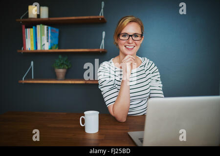 Fiducioso imprenditore femmina in ufficio sorridente in telecamera seduta con un laptop Foto Stock