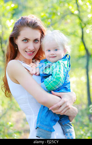 Madre mantiene il bambino in braccio su all'aperto, sorridente e guardando la telecamera Foto Stock