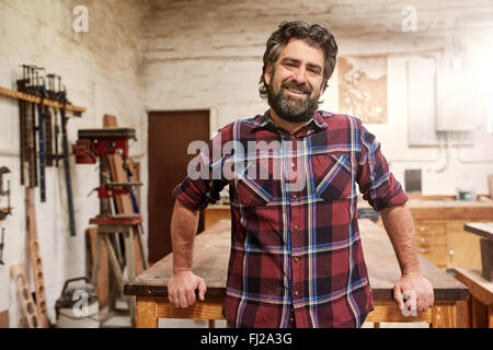 Sorridente barbuto artigiano nel suo studio di falegnameria Foto Stock