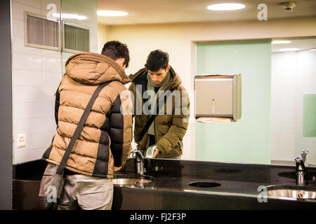 La riflessione del giovane di lavaggio delle mani in un bagno pubblico Foto Stock