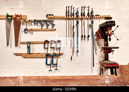 Parete di officina con strumenti in righe a fianco di un trapano verticale Foto Stock