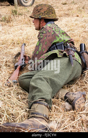 La seconda guerra mondiale la rievocazione. German Waffen SS soldato in dot camouflage uniforme, posa in erba, fucile in una mano. Close up. Foto Stock