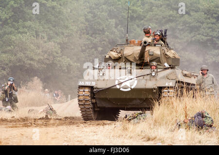 La seconda guerra mondiale la rievocazione. American medie serbatoio, M18 Hellcat, con supporto di fanteria, avanzante attraverso erba alta verso viewer durante la battaglia. Foto Stock