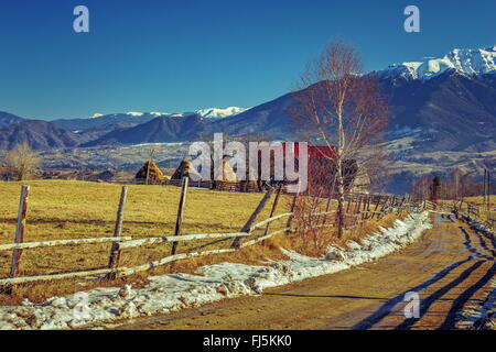 Montagna paesaggio rurale con tradizionale Rumena farm e fangoso country road durante l'inverno nelle valli delle montagne di Bucegi, B Foto Stock