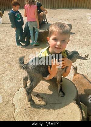 Ragazzo abbracciando una capra in uno zoo di animali domestici, Germania Foto Stock