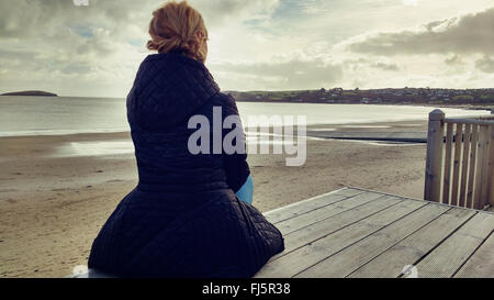 Giovane ed elegante donna seduta in legno sulla spiaggia Foto Stock