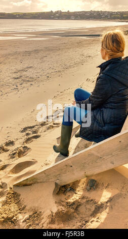 Bionda e giovane donna seduta sulle scale di cabine sulla spiaggia Foto Stock