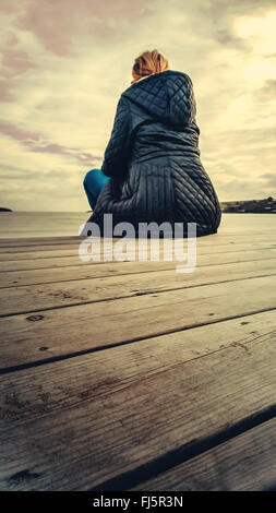 Giovane donna bionda che posa su pavimento di legno sulla spiaggia Foto Stock