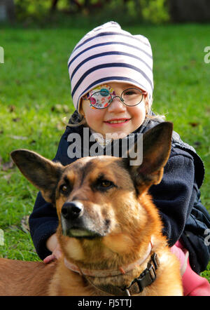 Razza cane (Canis lupus f. familiaris), bambina con occhio patch accarezzare un cane, Germania Foto Stock