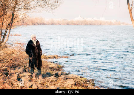 Una donna matura che indossa una calda pelliccia e un cappello di lana resta vicino al fiume Dnieper a Kiev, Ucraina, durante la stagione invernale Foto Stock