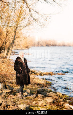 Una donna matura che indossa una calda pelliccia e un cappello di lana resta vicino al fiume Dnieper a Kiev, Ucraina, durante la stagione invernale Foto Stock