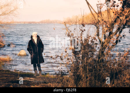 Una donna matura che indossa una calda pelliccia e un cappello di lana resta vicino al fiume Dnieper a Kiev, Ucraina, durante la stagione invernale Foto Stock