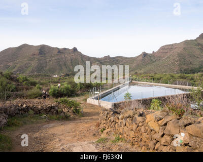 Il sentiero e bacino d'acqua con gli escursionisti in montagna sopra Santiago del Teide Tenerife Spagna, parte del fiore di mandorla escursione Foto Stock