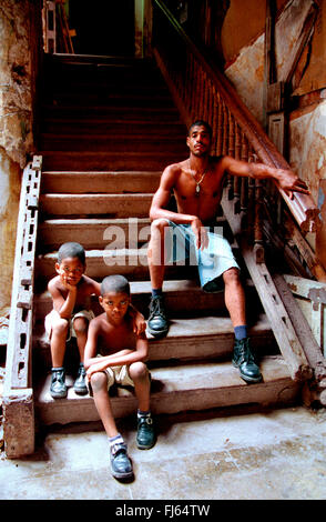 Padre con i suoi due figli, seduti su scale presso l'entrata della loro casa, Cuba Foto Stock