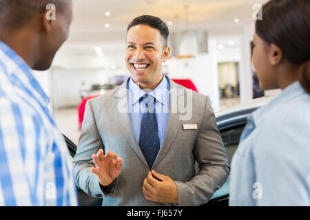 Bello il concessionario veicolo a parlare con i clienti in showroom Foto Stock