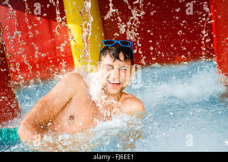 Uomo in tronchi swimmning sotto gli spruzzi di una fontana. Il calore d'estate. Foto Stock
