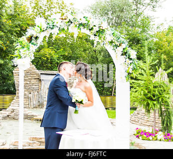 Primo bacio degli sposi sotto arco di nozze Foto Stock